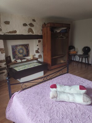 Una habitación con una cama, un armario de madera, un reloj de pared y una mesita con libros.