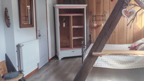 Een kamer met een houten vloer, een witte radiator, een houten kledingkast, een bed met een witte spreidek en een houten trap.