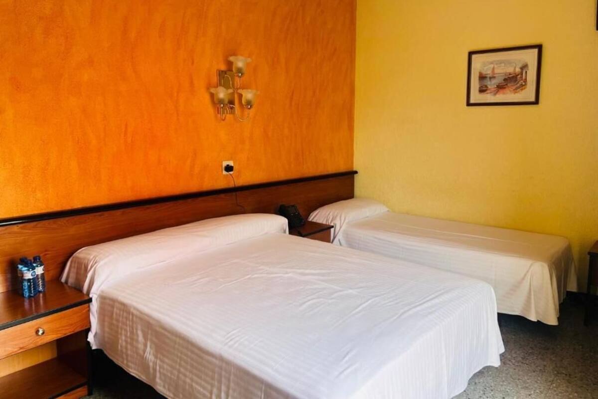 Una habitación de hotel con dos camas individuales, un cabecero de madera, una mesita de noche con una lámpara y un cuadro enmarcado en la pared.