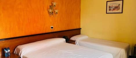 A hotel room with two single beds, a wooden headboard, a bedside table with a lamp, and a framed picture on the wall.