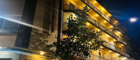 A multi-story hotel with balconies and a tree in front.