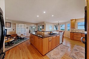 A spacious kitchen with wooden cabinets, a central island, and a dining area with a table and chairs. - #HabitueHomes - The Quail Ridge Overlook (Boise)