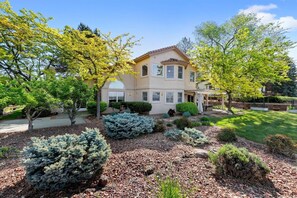 A two-story house with a patio, surrounded by landscaped gardens and trees. - #HabitueHomes - The Quail Ridge Overlook (Boise)