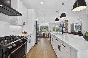 A modern kitchen with white cabinetry, a gas stove, pendant lighting, and a view to a living area. - Fresh Tracks @ Peak View Ridge (Winter Park)