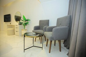 A modern living room with two grey armchairs, a glass coffee table, a white cabinet, a round mirror, and a potted plant. - Zamalek Romantic Nile Suite (Cairo Governorate)