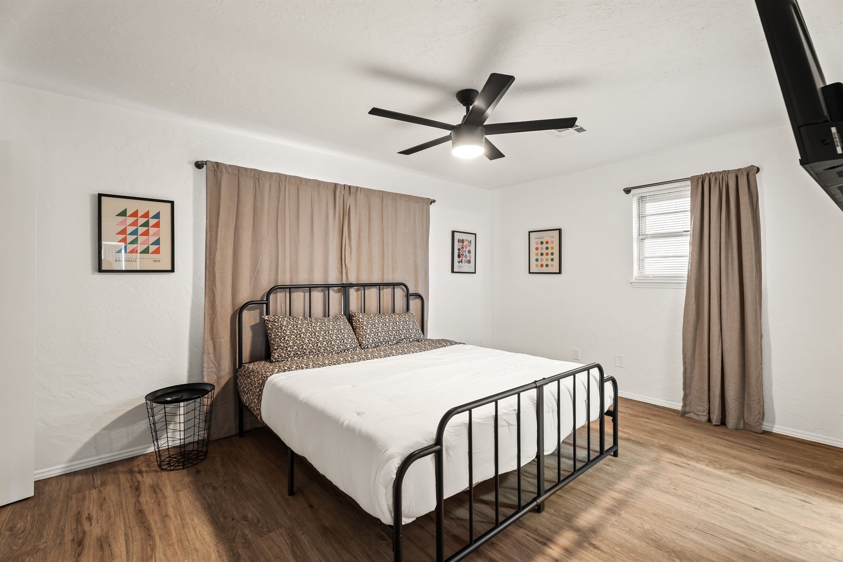 Un dormitorio con cama, ventilador de techo, ventana con cortinas y decoración en la pared.