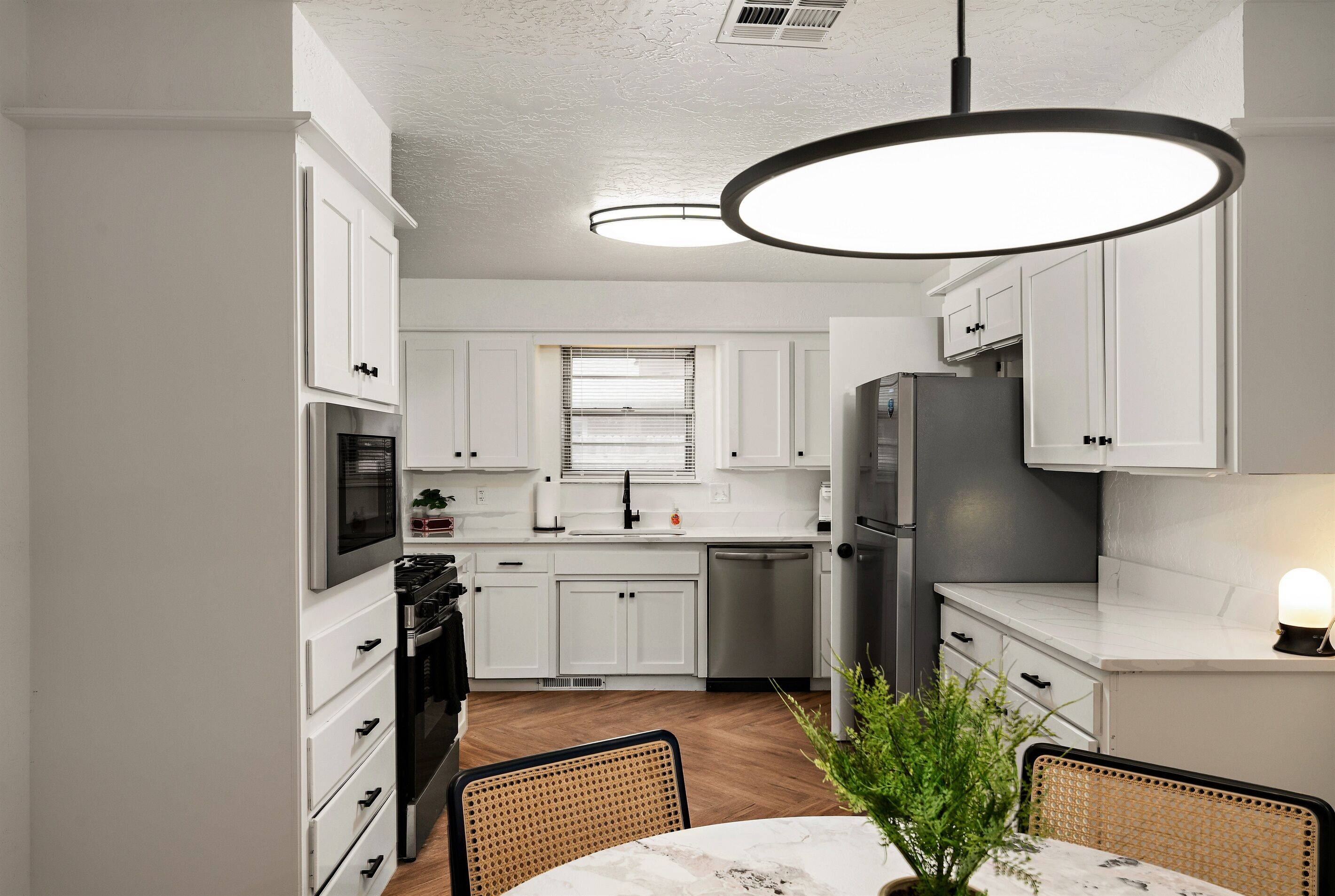 A modern kitchen with white cabinets, a dining area with a table and chairs, and a hanging light fixture.