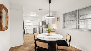 Moderni keittiö, jossa on valkoiset kaapit, pyöreä ruokapöytä mustilla tuoleilla ja riippuvalaisin.