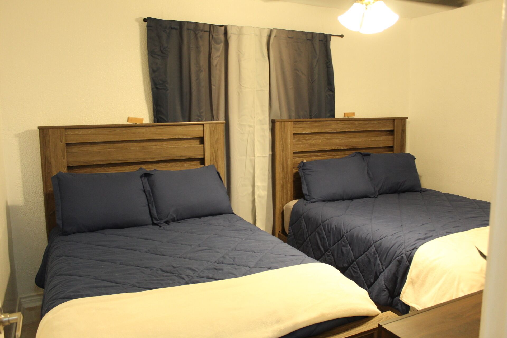 Deux lits simples avec des têtes de lit en bois, une fenêtre avec des rideaux et un luminaire au plafond.
