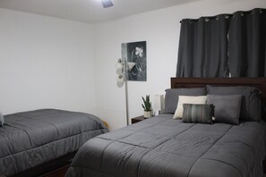 A bedroom with two beds, a nightstand, a lamp, a potted plant, and a painting on the wall. - A cozy and spacious 4bdrm near Kemah, Hobby Airport and NRG. Long stays welcome! (Houston)