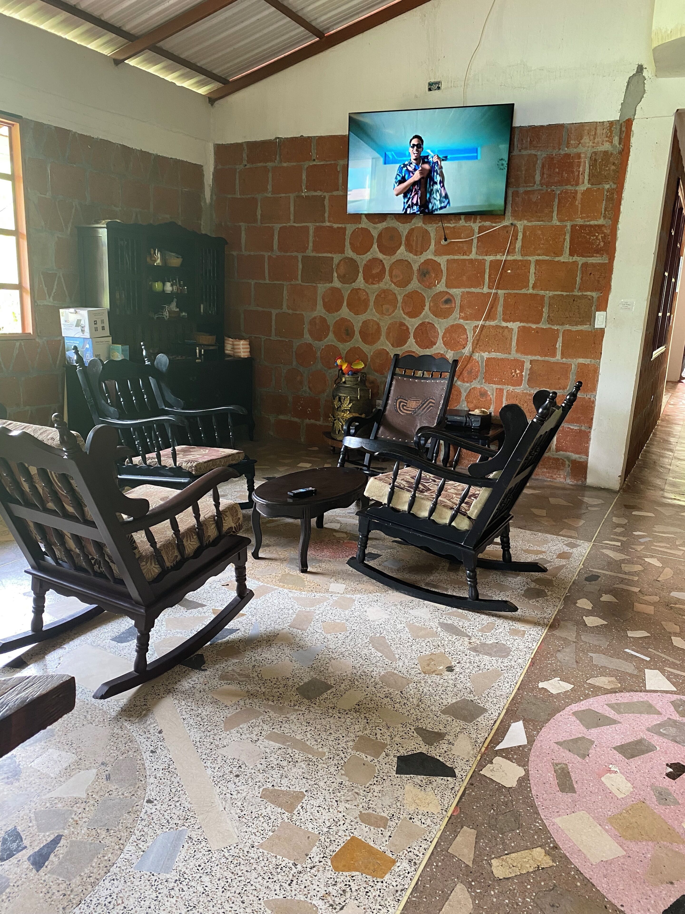 A living room with a TV mounted on the wall, a patterned floor, and a brick wall.