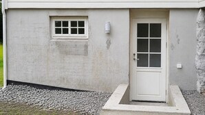 Un bâtiment à l’extérieur blanc, doté d’une petite fenêtre et d’une porte avec un panneau de verre.