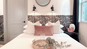 A bedroom with a bed, a round mirror, two wall-mounted lights, a bedside table with a vase, and a window with curtains. - Dallas Downtown, FIFA Close to All the FUN! (Dallas)