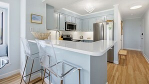 Cozinha moderna com ilha central, eletrodomésticos de aço inoxidável e cadeiras transparentes.