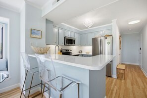 A modern kitchen with a central island, stainless steel appliances, and clear chairs. - Beachside Coastal Retreat | Pool, Tennis & Walkable Beach Access (Atlantic Beach)