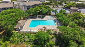 Resort com piscina rodeada por vegetação exuberante, área de estacionamento e edifícios com vista para o oceano.
