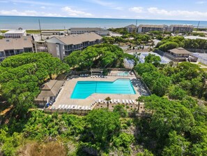 A resort with a swimming pool surrounded by lush greenery, a parking area, and buildings with a view of the ocean. - Beachside Coastal Retreat | Pool, Tennis & Walkable Beach Access (Atlantic Beach)