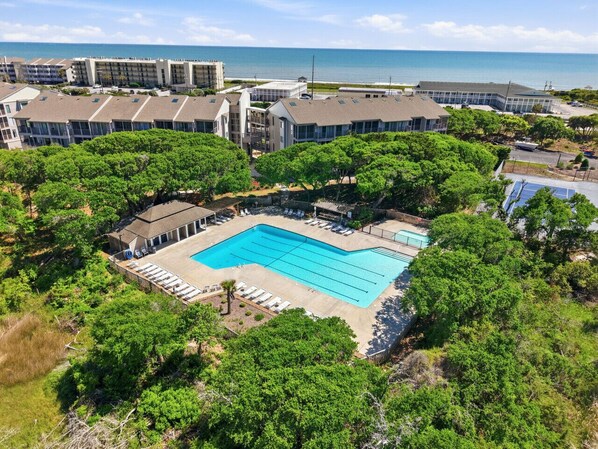 A swimming pool surrounded by trees, with buildings in the background. - Beachside Coastal Retreat | Pool, Tennis & Walkable Beach Access (Atlantic Beach)