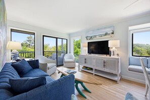 A spacious living room with a sofa, chairs, a TV, and a balcony with a view. - Beachside Coastal Retreat | Pool, Tennis & Walkable Beach Access (Atlantic Beach)