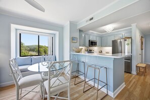 A modern kitchen with a bar area, a dining table with chairs, and a view of the outdoors. - Beachside Coastal Retreat | Pool, Tennis & Walkable Beach Access (Atlantic Beach)