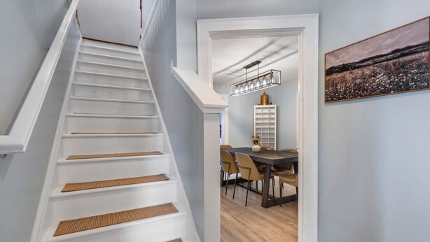 A staircase with white steps and a wooden handrail, leading to a dining area with a table and chairs. - The Retreat at Harpers Ferry (Bolivar)