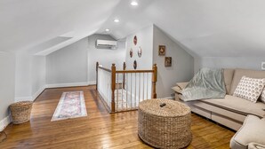 A loft-style room with a wooden floor, a sofa, a woven ottoman, a staircase, and a railing. - The Retreat at Harpers Ferry (Bolivar)