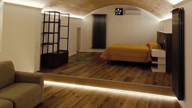Een kamer met een schuine plafond, een bed met een gele sprei, een metalen plank en een houten vloer.
