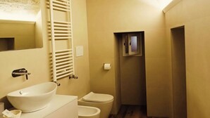 Een kleine badkamer met een wastafel, twee toiletten, een handdoekhouder en een klein raam.