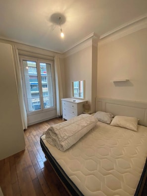 Une chambre avec un grand lit, une commode, un miroir et une fenêtre donnant sur des balcons.