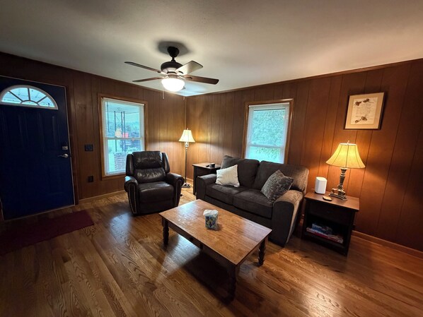 A living room with a ceiling fan, a leather chair, a sofa with cushions, a wooden coffee table, and two lamps. - Cozy 2 bedroom house near New River, game room, WiFi, brand new kitchen/bathroom (Galax)