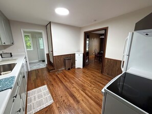 A kitchen with wooden flooring, white cabinets, a refrigerator, and a dining area with a chair and table. - Cozy 2 bedroom house near New River, game room, WiFi, brand new kitchen/bathroom (Galax)