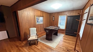 A room with wooden walls, a foosball table, a chair, and a painting on the wall. - Cozy 2 bedroom house near New River, game room, WiFi, brand new kitchen/bathroom (Galax)