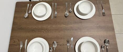 A rectangular dining table with four sets of white plates, cutlery, and bowls, surrounded by four chairs.