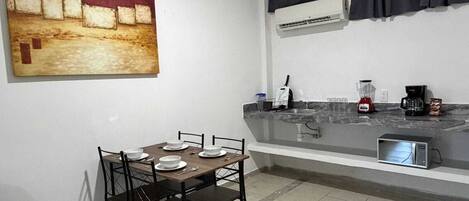 A compact kitchen with a dining table, chairs, a countertop with appliances, and a painting on the wall.
