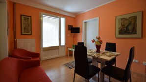 Una sala de estar con sofá, mesa de comedor, sillas, televisor y obras de arte en las paredes.