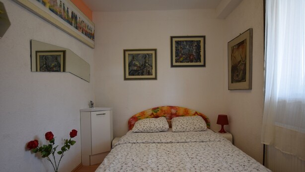 Un dormitorio con cama, mesita de noche, lámpara, cómoda, espejo y un florero con flores.