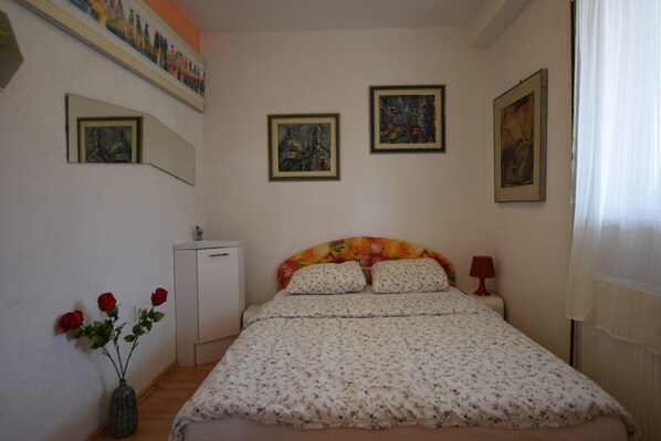 A bedroom with a bed, a bedside table, a lamp, a dresser, a mirror, and a vase with flowers. - Spacious Apartment With Terrace and Outdoor Kitchen With sea View (Opatija)