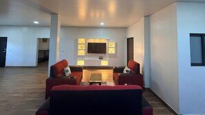 A spacious living area with a flat-screen TV mounted on the wall, a wooden coffee table, and two red sofas.