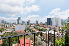 A cityscape with modern buildings, a balcony with a railing, and a clear sky. - Volcano Sunrise 1009, new 1-bedroom apartment with rooftop pool & gym nr airport (San José)