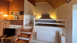 A cozy room with a bunk bed, wooden shelves with books, a desk with a computer, and a staircase. - La Petite Maison (Peyzac-le-Moustier)
