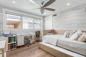 Ein Schlafzimmer mit einem Bett, einem Schreibtisch, einem Bücherregal, einem Deckenventilator und einem Fenster.