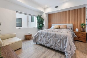 Ein modernes Schlafzimmer mit einem Bett, einem Holzkopfstück, einem Fenster, einer Pflanze und einem Nachttisch.
