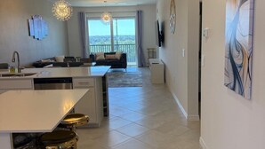 A modern kitchen with a bar area, a dining area with a sofa, and a large window with a view. - 2-bedroom apartment in delightful Venice with balcony, cool AC and gym pool! (Venice)