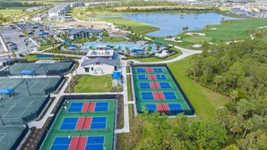 An aerial view of a golf course with multiple tennis courts, a swimming pool, and a large body of water. - 2-bedroom apartment in delightful Venice with balcony, cool AC and gym pool! (Venice)