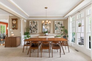 Une salle à manger avec une table et des chaises en bois, un lustre et des étagères murales ornées de plantes.