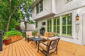 Une terrasse dotée de mobilier d’extérieur, d’un grand bac à fleurs et d’un bâtiment aux volets verts.