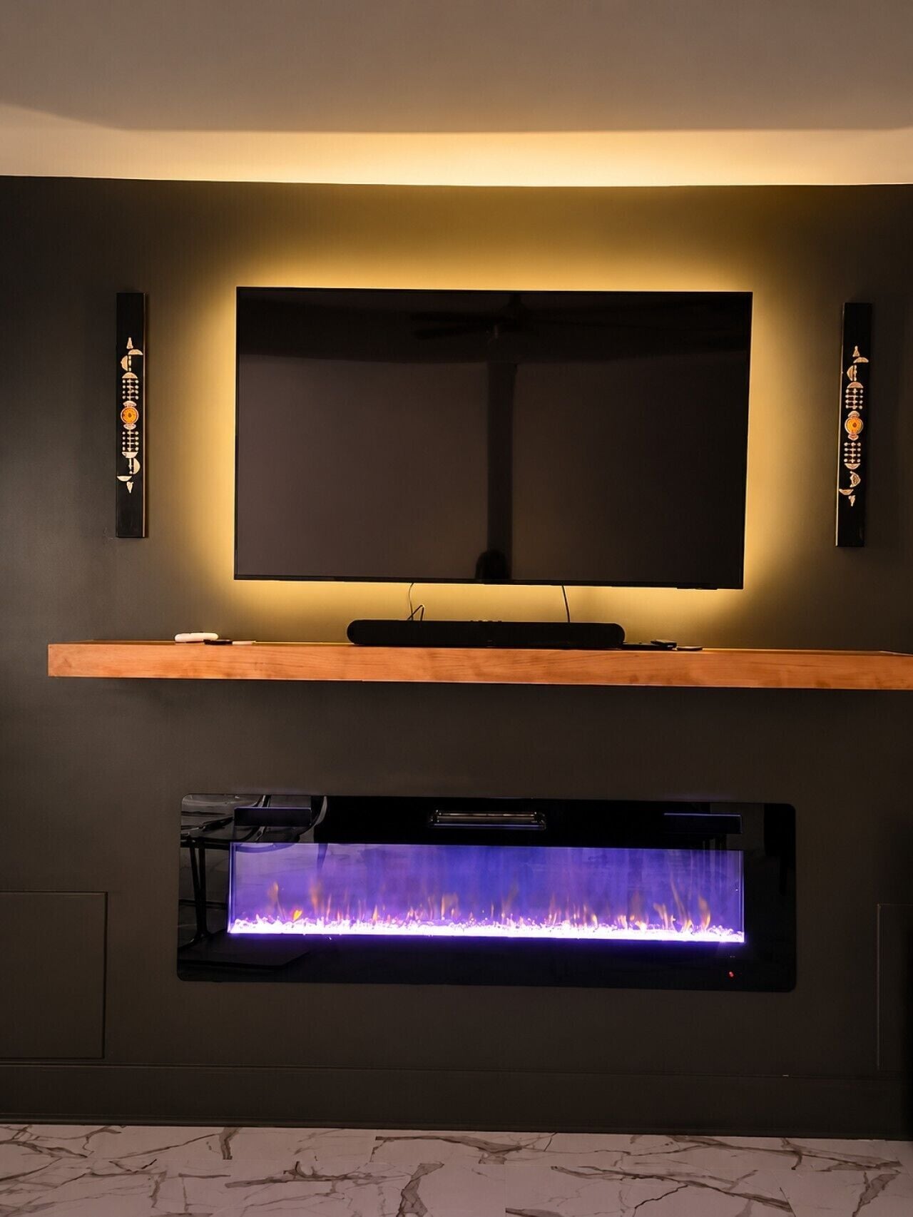 A flat-screen TV mounted on a wall above a wooden shelf, with a fireplace below.