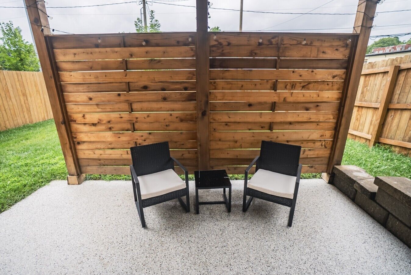 An outdoor patio area with two chairs and a small table, surrounded by a wooden fence.