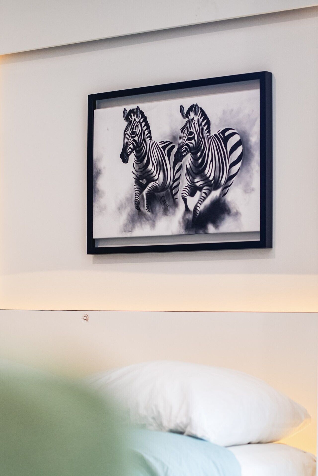 Una obra enmarcada con dos cebras colgada sobre una cama, con un almohábil blanco y una manta verde.