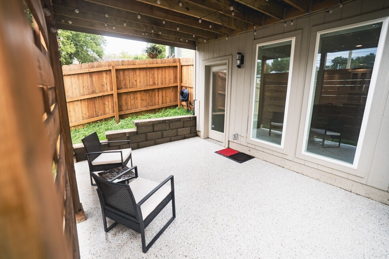 An outdoor patio area with a wooden fence, a seating arrangement, and a door leading to a covered space.